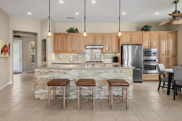 a kitchen with kitchen island stainless steel appliances a refrigerator a stove a sink cabinets and chairs