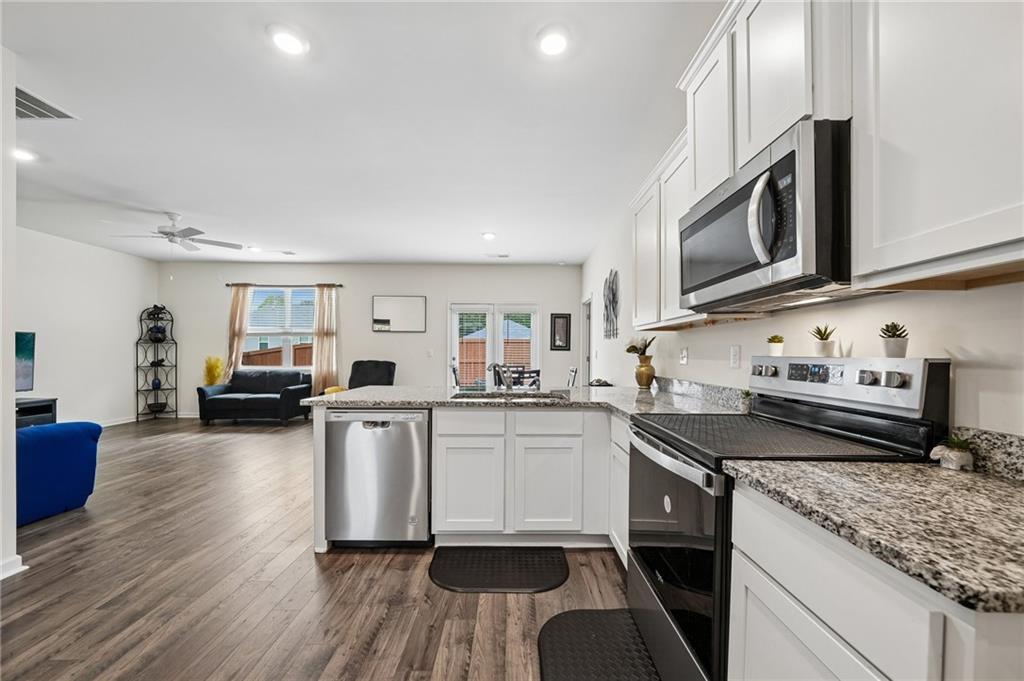 8592 Seabiscuit Road Lithonia, GA 30058 - Photo 8 of 25 a kitchen with stainless steel appliances granite countertop a stove top oven a sink dishwasher a dining table and chairs with wooden floor