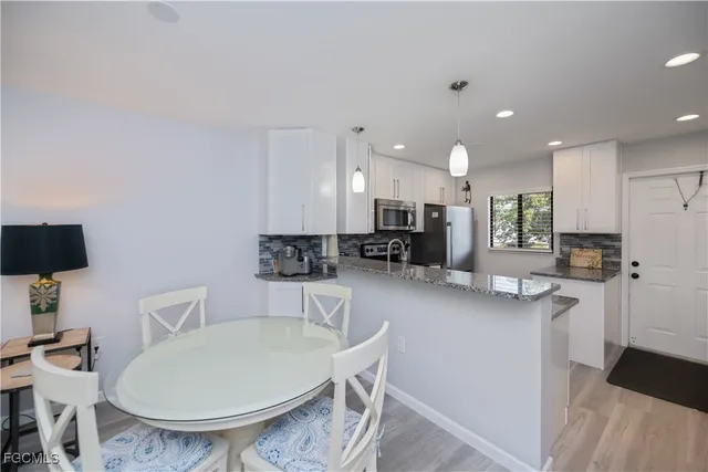 a kitchen with stainless steel appliances kitchen island granite countertop a sink a stove a refrigerator a microwave oven with white cabinets and wooden floor