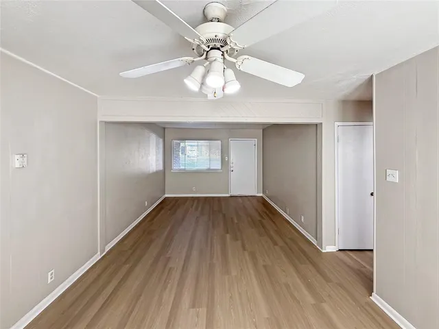 an empty room with wooden floor a ceiling fan and kitchen view