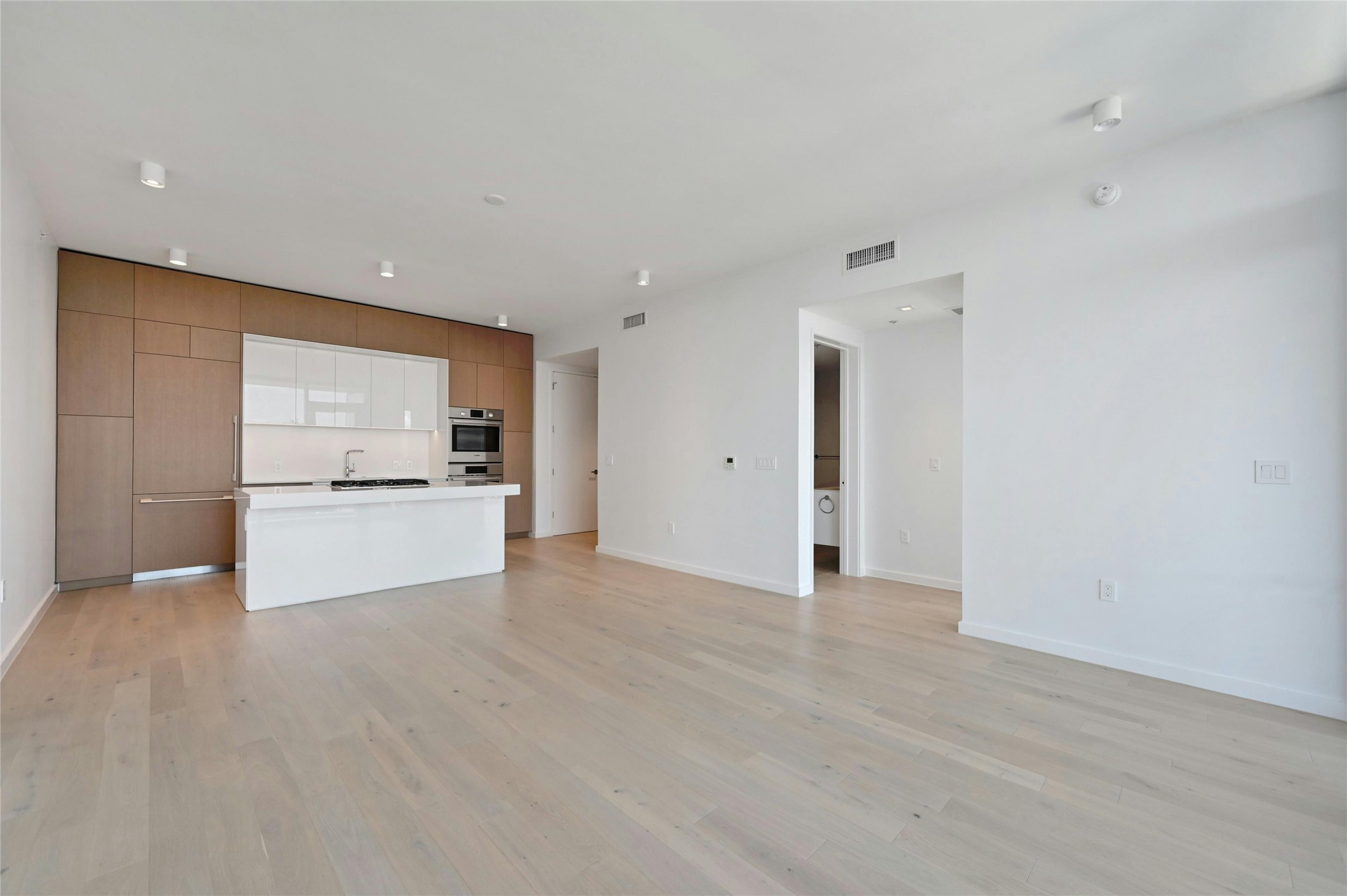 313 West 17th Street, Unit 2101 Austin, TX 78701 - Photo 3 of 36 Sophisticated open-concept kitchen featuring sleek Bosch appliances, integrated wood-paneled cabinetry, and a glossy white island ideal for casual dining or entertaining—all seamlessly connected to the main living space with clean, modern lines.