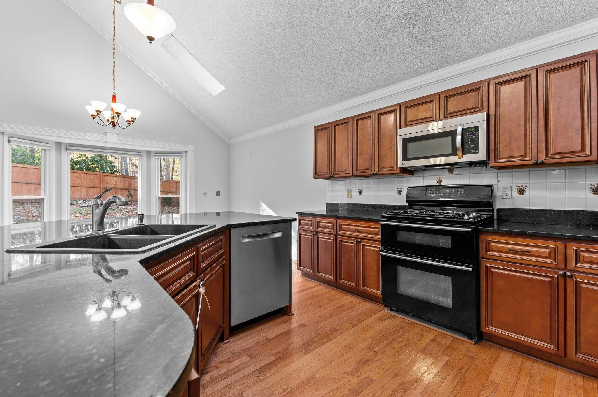 5808 Glenfiddich Way Raleigh, NC 27613 - Photo 44 of 64 a kitchen with stainless steel appliances granite countertop wooden cabinets a stove a sink and a microwave