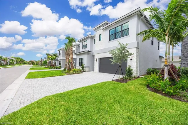a view of yellow house with a big yard and potted plants