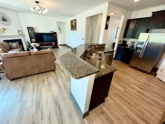 a living room with stainless steel appliances furniture a fireplace a flat screen tv and a wooden floor