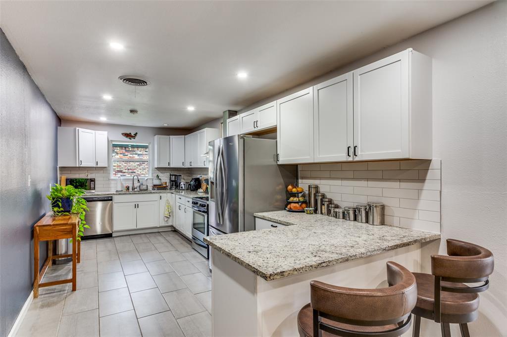6921 Valhalla Road Fort Worth, TX 76116 - Photo 12 of 25 Kitchen featuring white cabinets, backsplash, light stone counters, a breakfast bar, and a peninsula