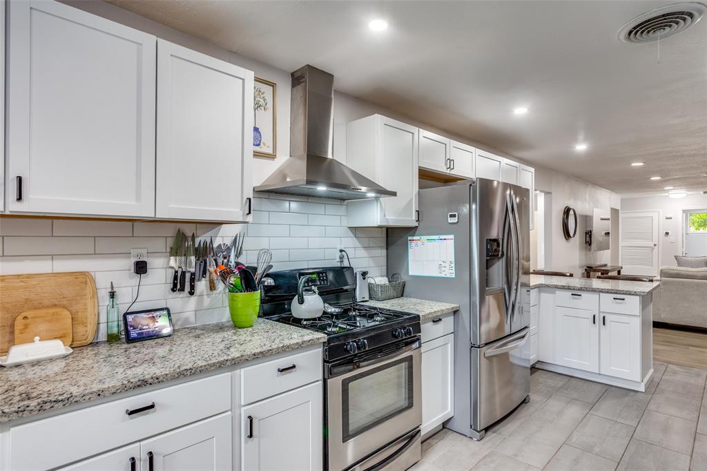 6921 Valhalla Road Fort Worth, TX 76116 - Photo 14 of 25 Kitchen featuring stainless steel appliances, wall chimney exhaust hood, light stone countertops, white cabinets, and a peninsula
