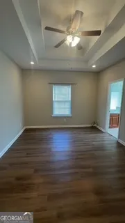 an empty room with wooden floor chandelier fan and windows