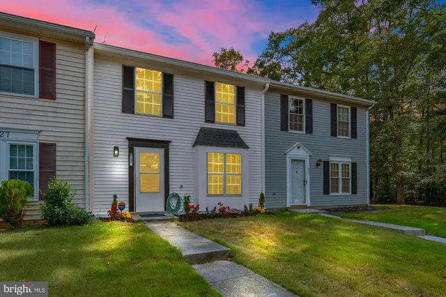 a front view of house and yard with swimming pool and trees in the background