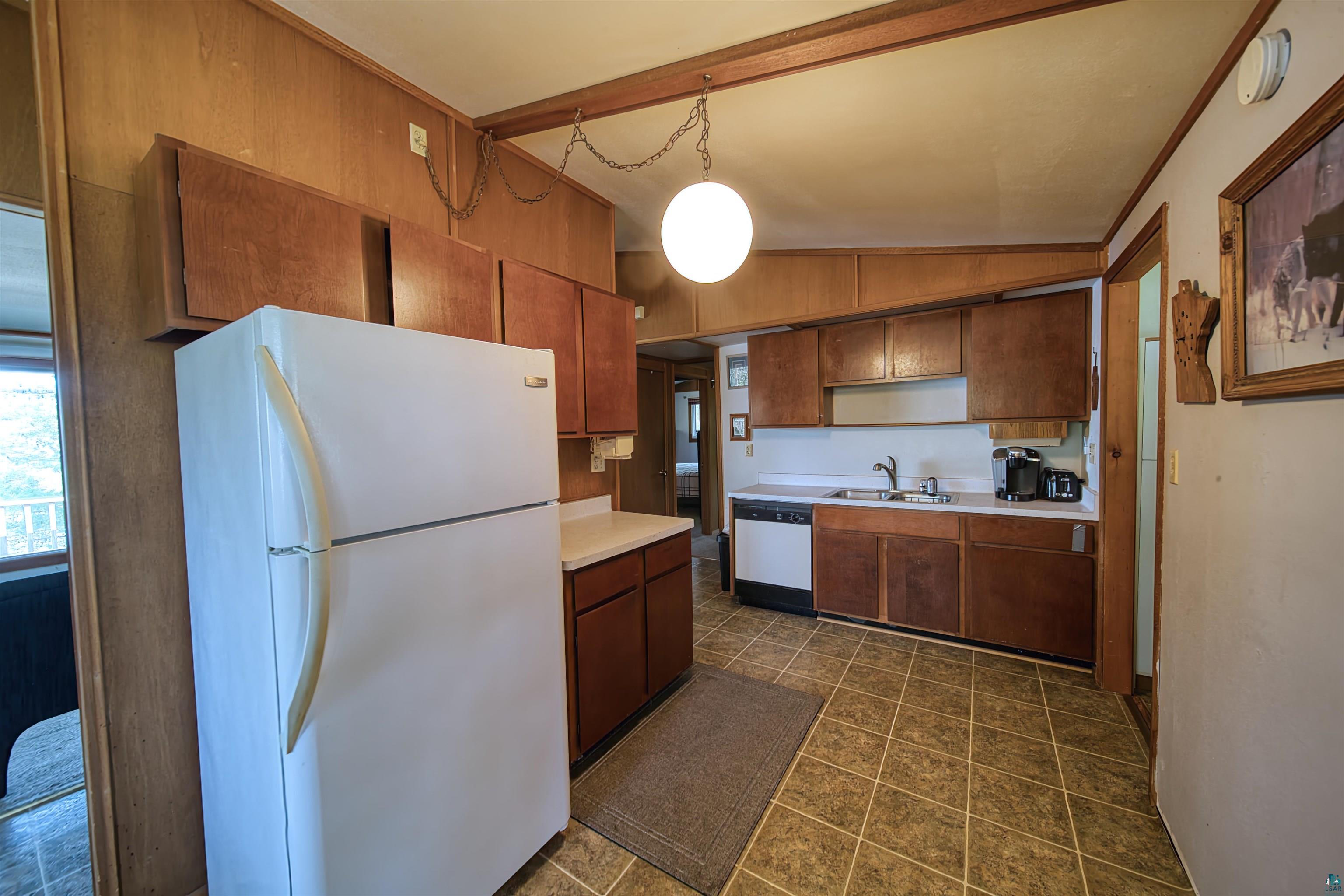 Kitchen featuring white appliances, vaulted ceiling, decorative light fixtures, dark tile flooring, and sink