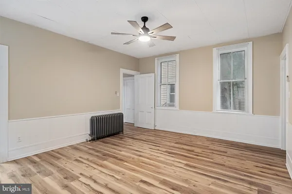 a view of an empty room with wooden floor and a ceiling fan