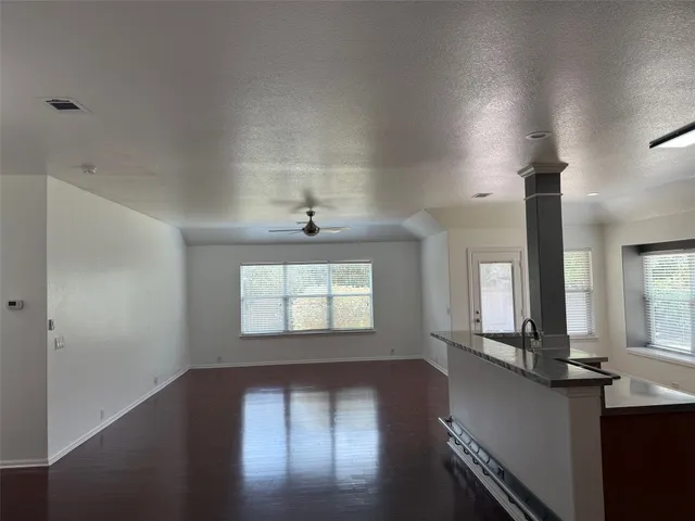 a view of an empty room with wooden floor and a kitchen