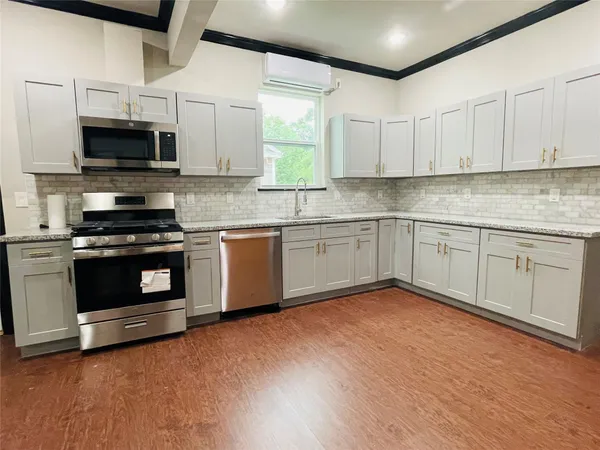 a kitchen with stainless steel appliances granite countertop a stove top oven a sink dishwasher and white cabinets with wooden floor