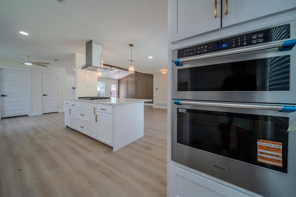 142 Ridgegate Drive Garland, TX 75040 - Photo 13 of 26 Modern kitchen featuring a central island with a gas cooktop, stainless steel range hood, white cabinetry with gold-tone hardware, and built-in stainless steel double ovens