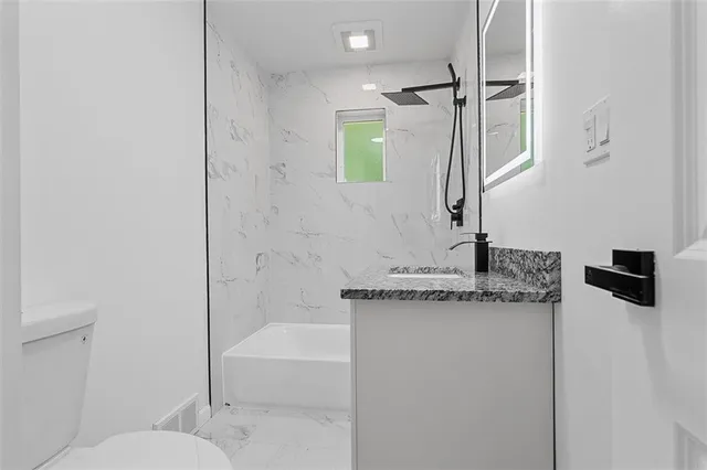 a bathroom with a granite countertop sink a toilet and shower