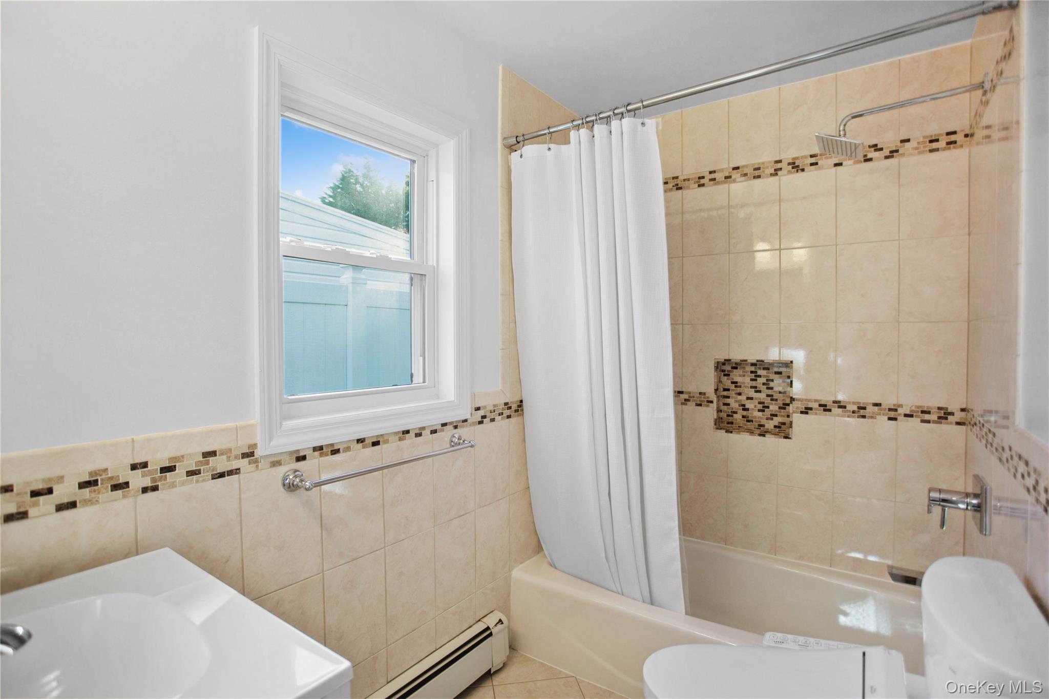 110 Hampton Way Merrick, NY 11566 - Photo 15 of 24 Full bath featuring shower / bathtub combination with curtain, baseboard heating, tile walls, a wainscoted wall, and tile patterned floors