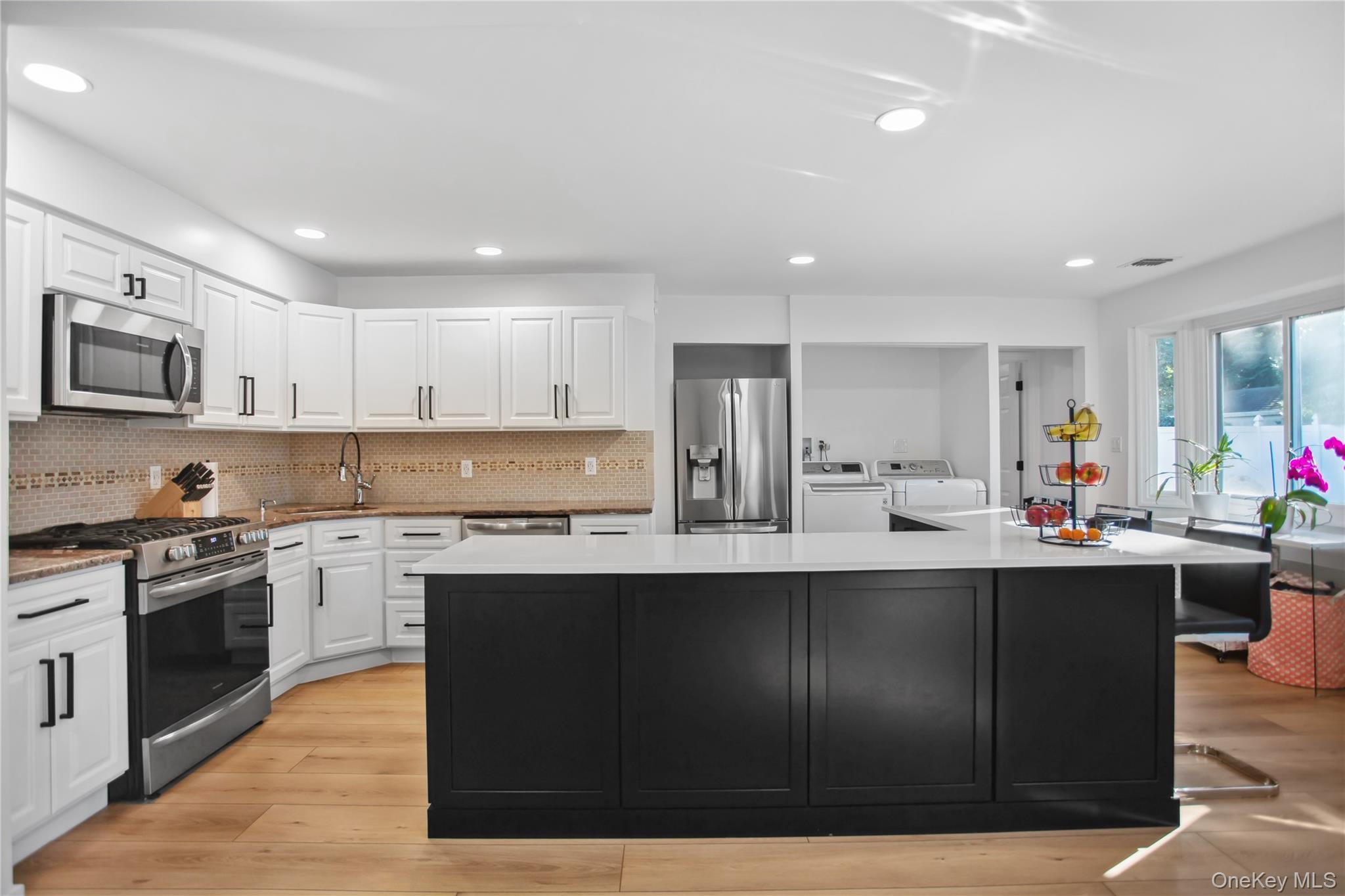 110 Hampton Way Merrick, NY 11566 - Photo 7 of 24 Kitchen featuring dark cabinetry, appliances with stainless steel finishes, light wood finished floors, independent washer and dryer, and white cabinets