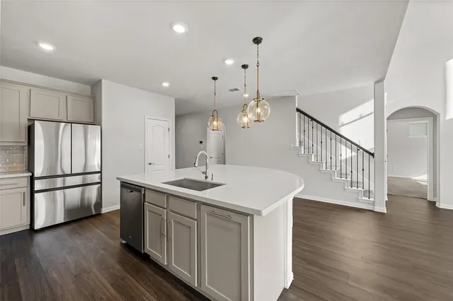 a kitchen with stainless steel appliances granite countertop a refrigerator a sink dishwasher a stove and a dining table with wooden floor