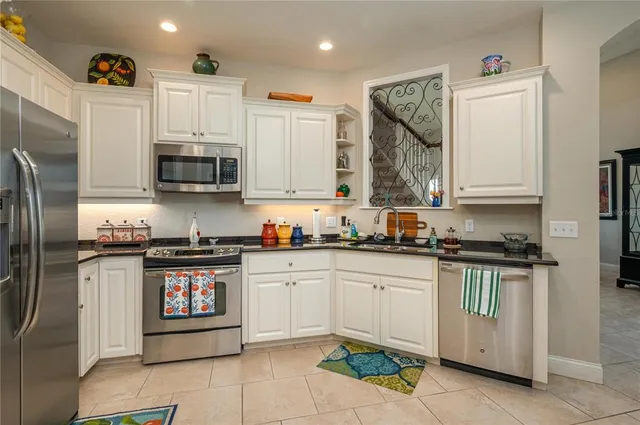 a kitchen with stainless steel appliances granite countertop a stove top oven a sink a refrigerator and white cabinets