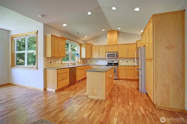 a kitchen with stainless steel appliances granite countertop a refrigerator a sink dishwasher and a stove with wooden floor