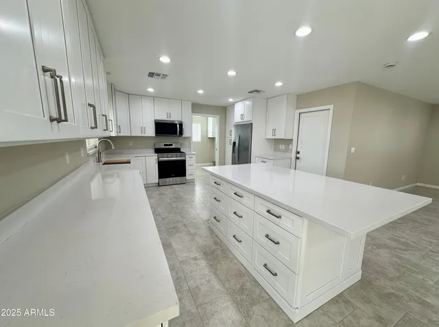 a large white kitchen with kitchen island a sink stainless steel appliances and cabinets
