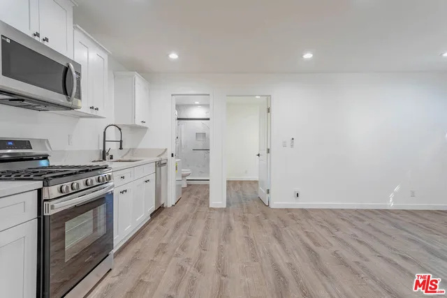 a kitchen with granite countertop a stove top oven a sink dishwasher a refrigerator and white cabinets with wooden floor