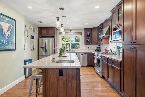 a kitchen with stainless steel appliances granite countertop a refrigerator a sink dishwasher a stove and a dining table with wooden floor