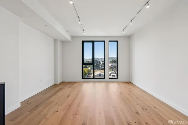 a view of an empty room with wooden floor and a window