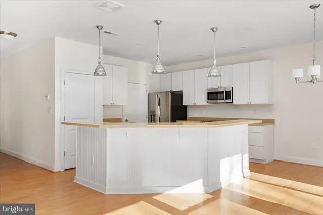 a kitchen with stainless steel appliances a refrigerator a sink dishwasher a stove and white cabinets with wooden floor