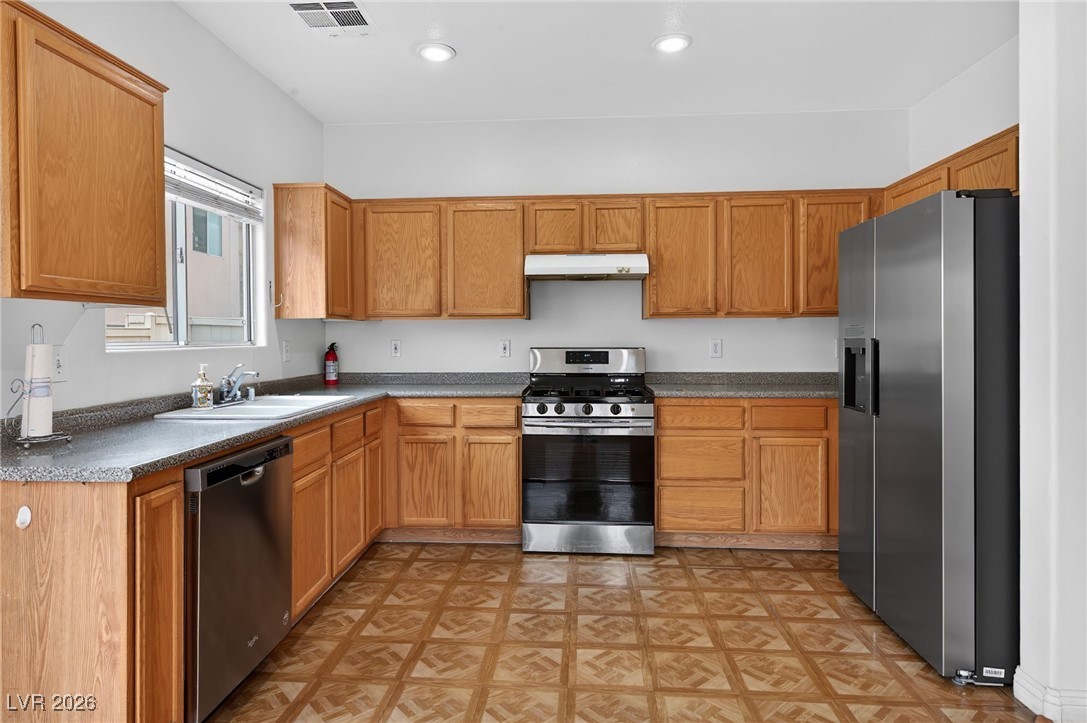8038 Kings Ransom Street Las Vegas, NV 89139 - Photo 11 of 38 Kitchen featuring appliances with stainless steel finishes, under cabinet range hood, brown cabinetry, light floors, and recessed lighting