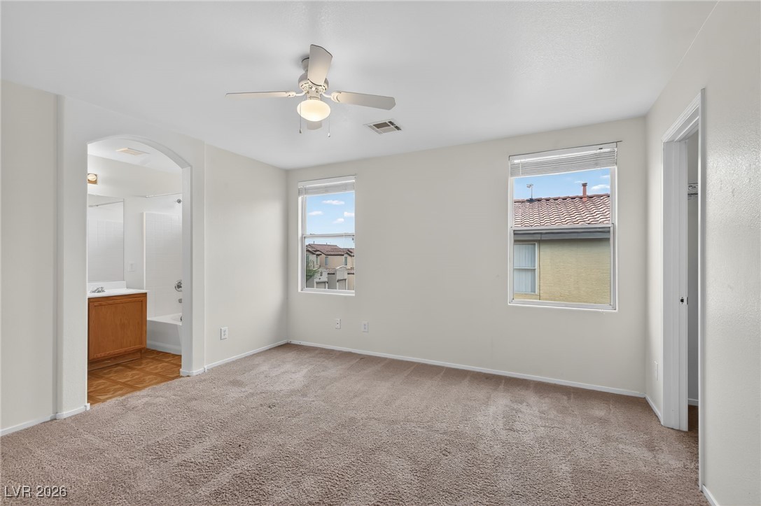 8038 Kings Ransom Street Las Vegas, NV 89139 - Photo 14 of 38 Unfurnished bedroom with multiple windows, light colored carpet, ceiling fan, and connected bathroom