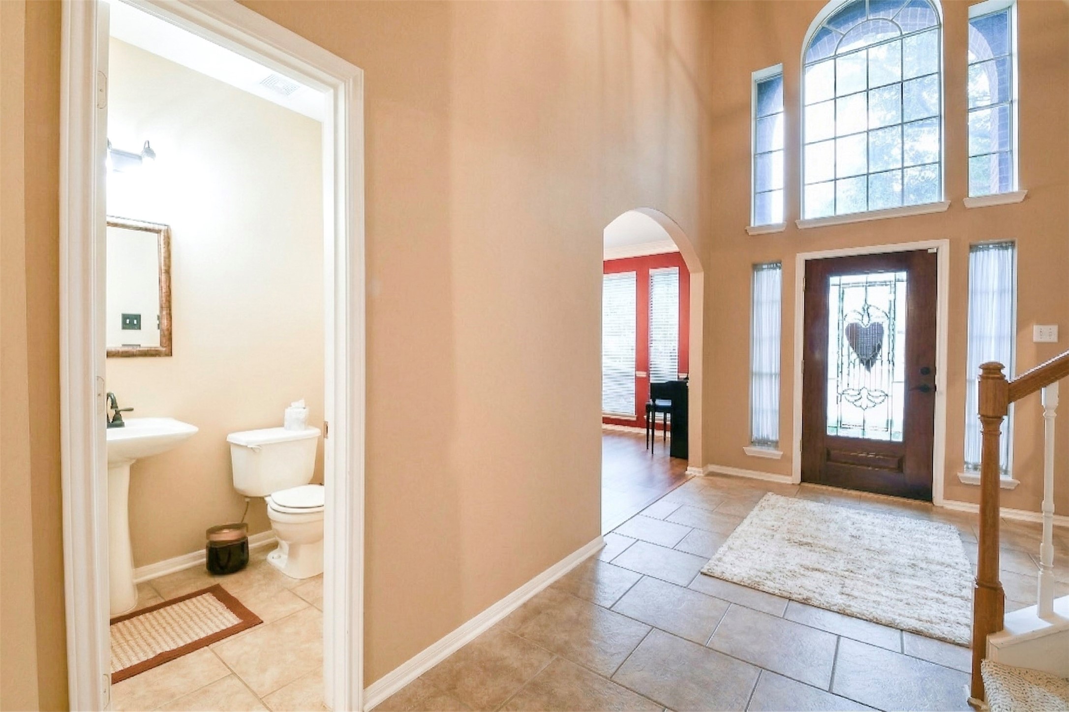 20423 Forest Drive Spring, TX 77388 - Photo 7 of 49 This photo showcases a bright entryway with a high ceiling and large arched window, a wooden front door with decorative glass, and tiled flooring. To the left is a small powder room with a pedestal sink and toilet. An archway leads to the dining room with large windows.