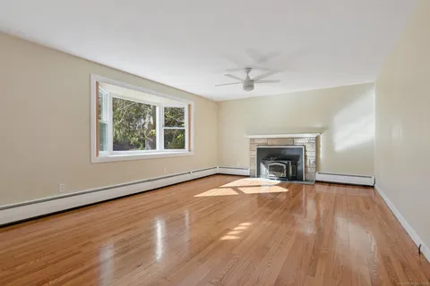 a view of an empty room with wooden floor fireplace and a window