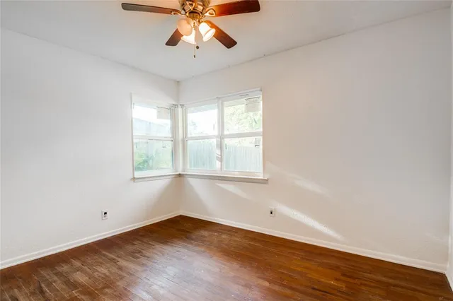 an empty room with wooden floor chandelier fan and windows