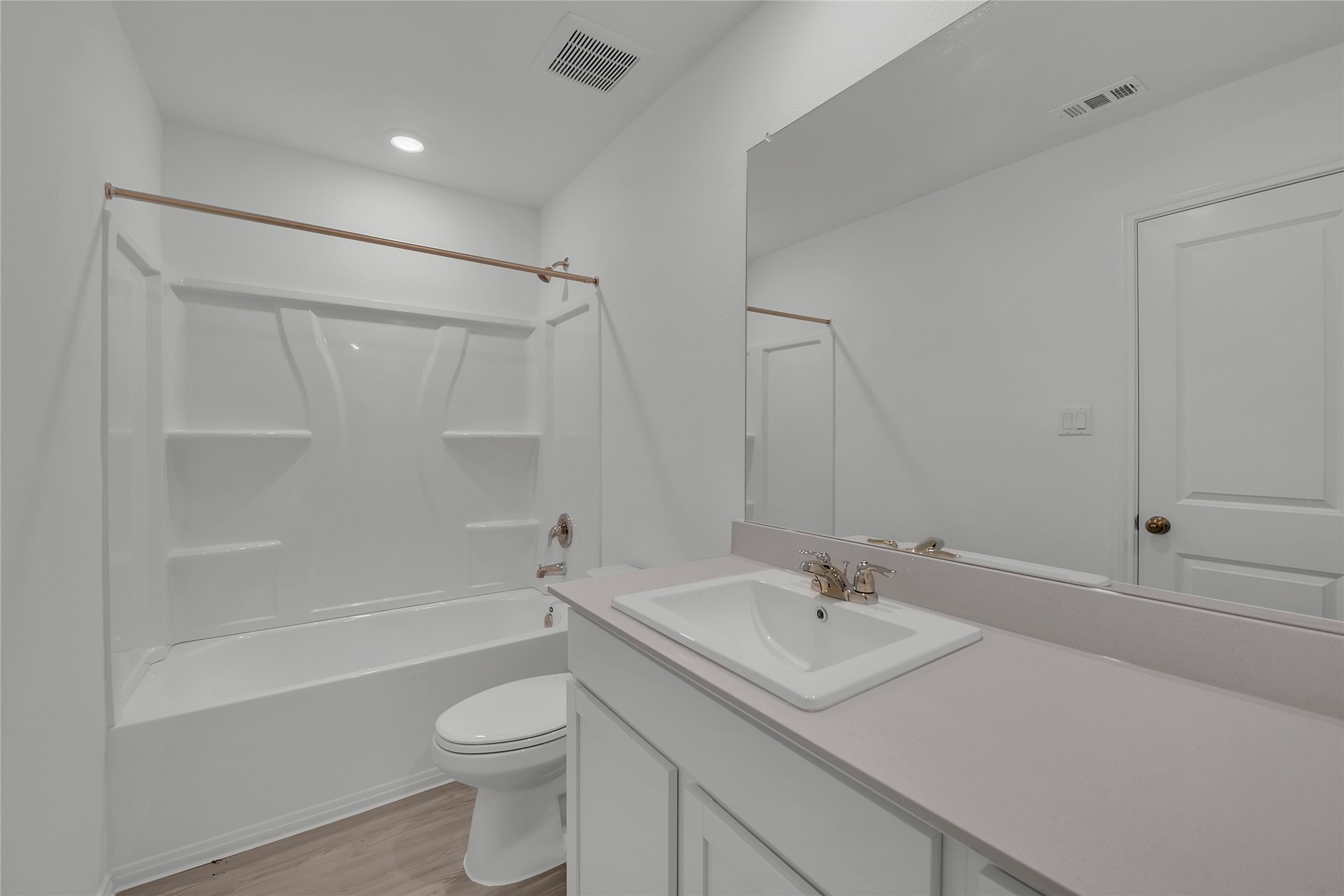 309 Marty Allen Loop Jarrell, TX 76537 - Photo 17 of 33 Bathroom featuring a white integrated tub and shower unit, a vanity with a light-toned countertop and integrated sink, a large wall-mounted mirror, and wood-finish flooring