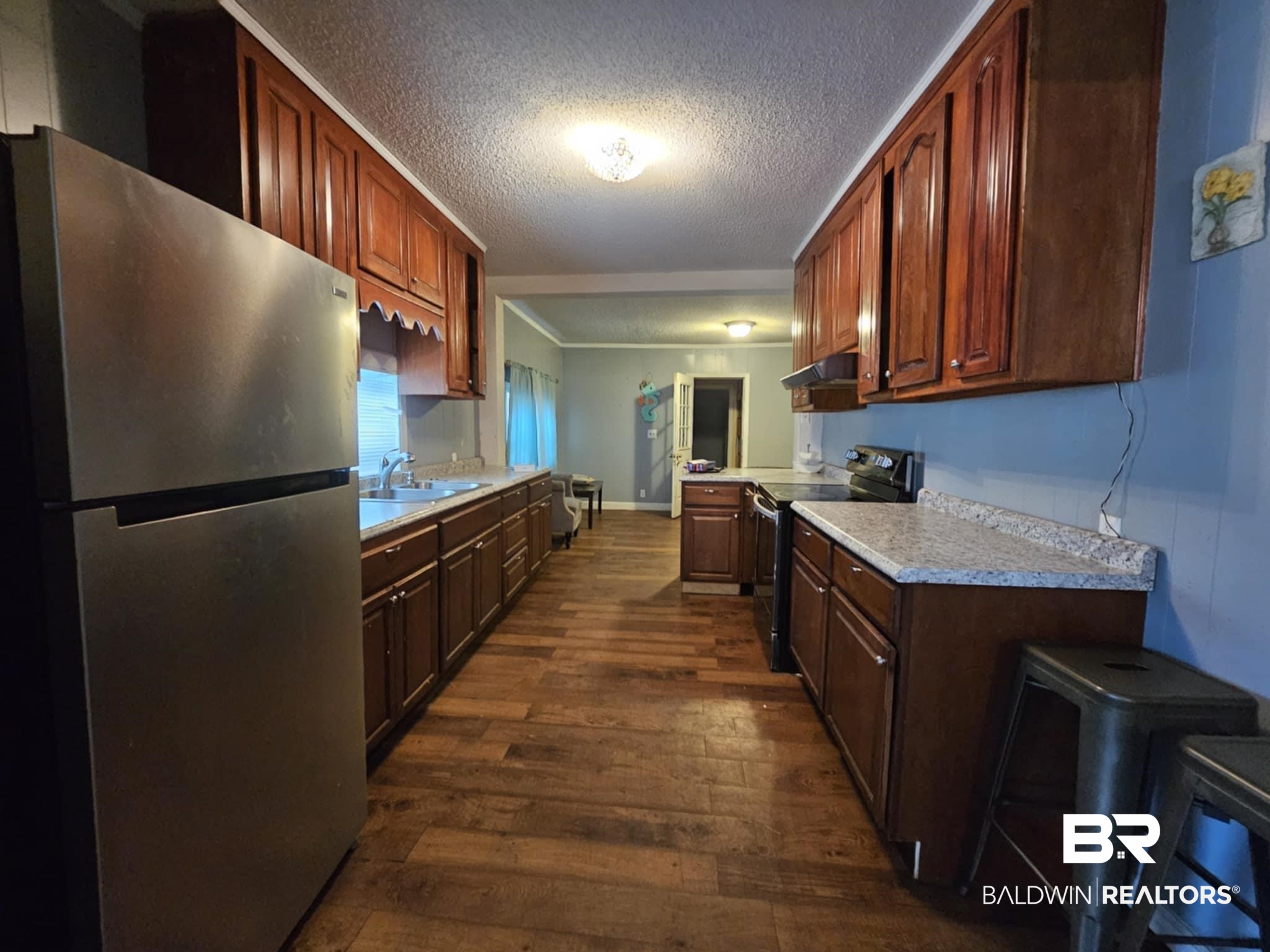 Kitchen featuring light countertops, appliances with stainless steel finishes, dark wood-type flooring, a sink, and under cabinet range hood
