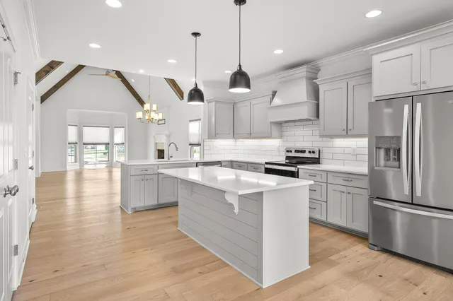 a kitchen with stainless steel appliances granite countertop a refrigerator a sink dishwasher a stove and white cabinets with wooden floor