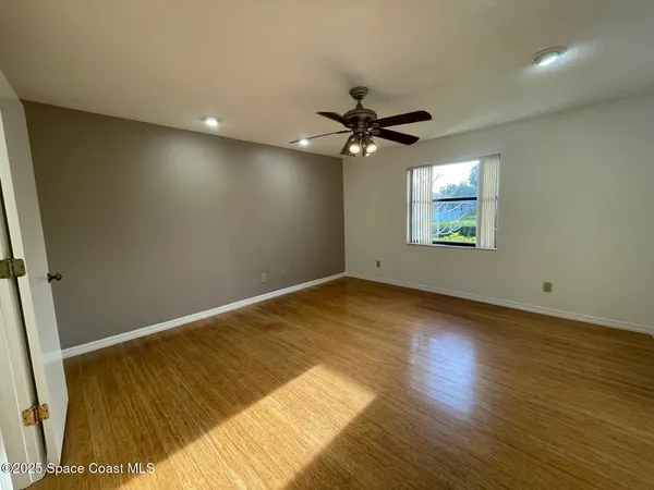 an empty room with wooden floor fan and windows