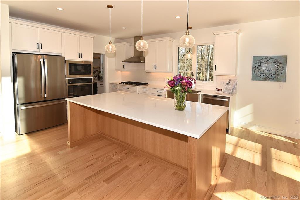 a kitchen with stainless steel appliances kitchen island granite countertop a refrigerator a sink dishwasher and a dining table with wooden floor
