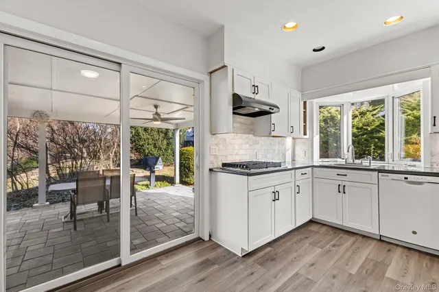 a kitchen with granite countertop a stove a sink and white cabinets with wooden floor next to windows