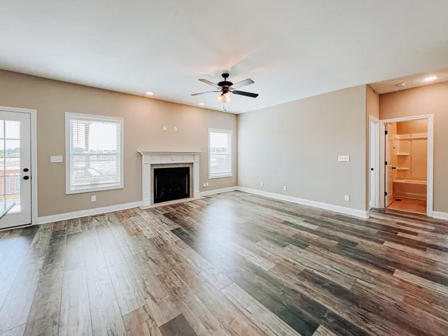 an empty room with wooden floor chandelier fan and windows