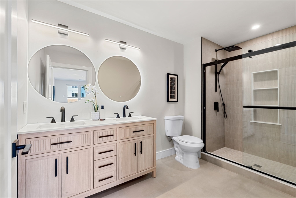 27 Guild Street, Unit 102 Boston, MA 02119 - Photo 16 of 29 a bathroom with a double vanity sink toilet mirror and shower