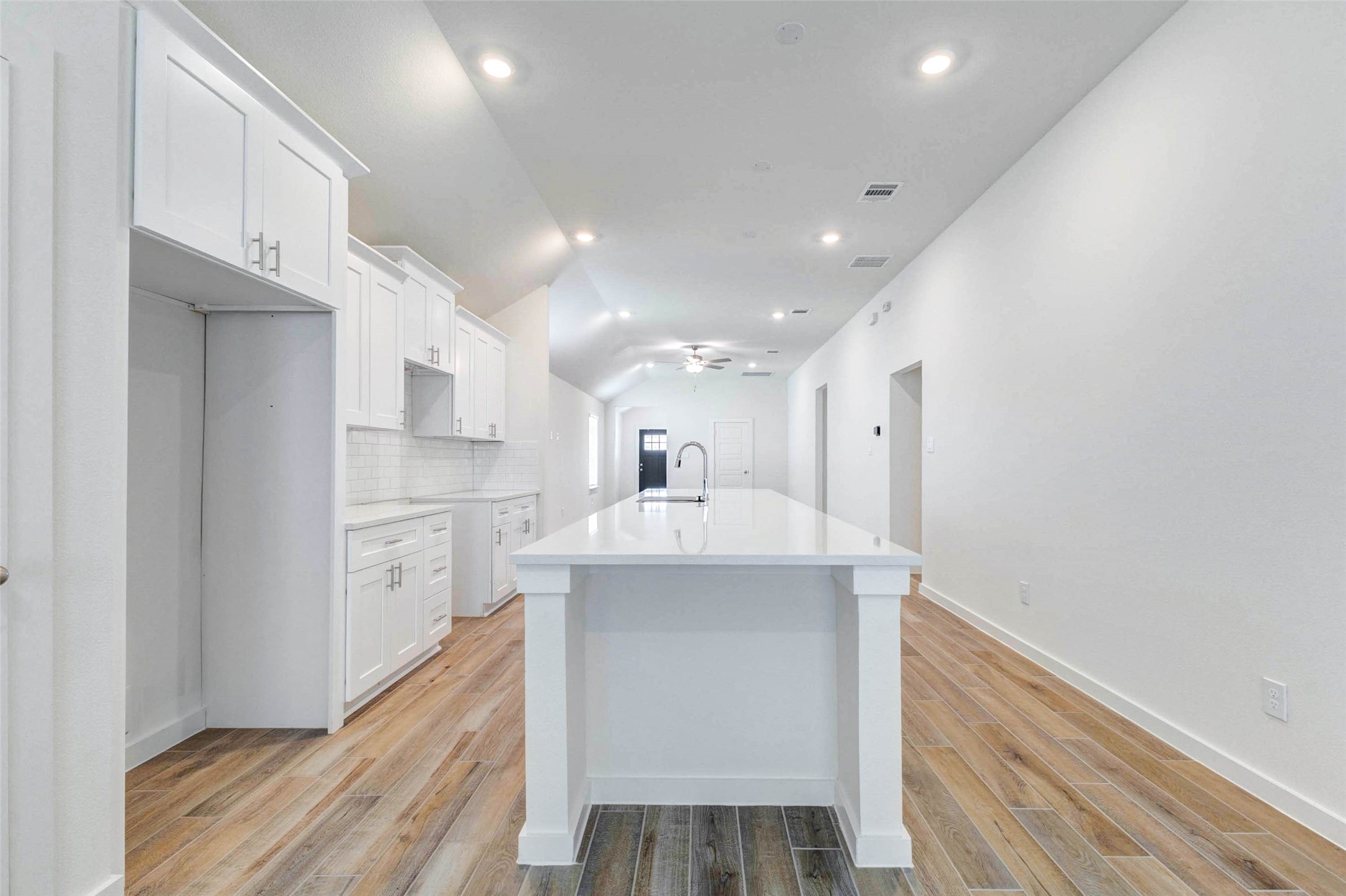 6475 Escondido Drive Rosharon, TX 77583 - Photo 15 of 32 This kitchen view showcases the oversized island, white cabinetry, recessed lighting, and long, open layout. The wood-look tile adds warmth while the clean white finishes keep the space bright and modern. With easy connection to the living area, this kitchen is designed for everyday comfort and entertaining.
