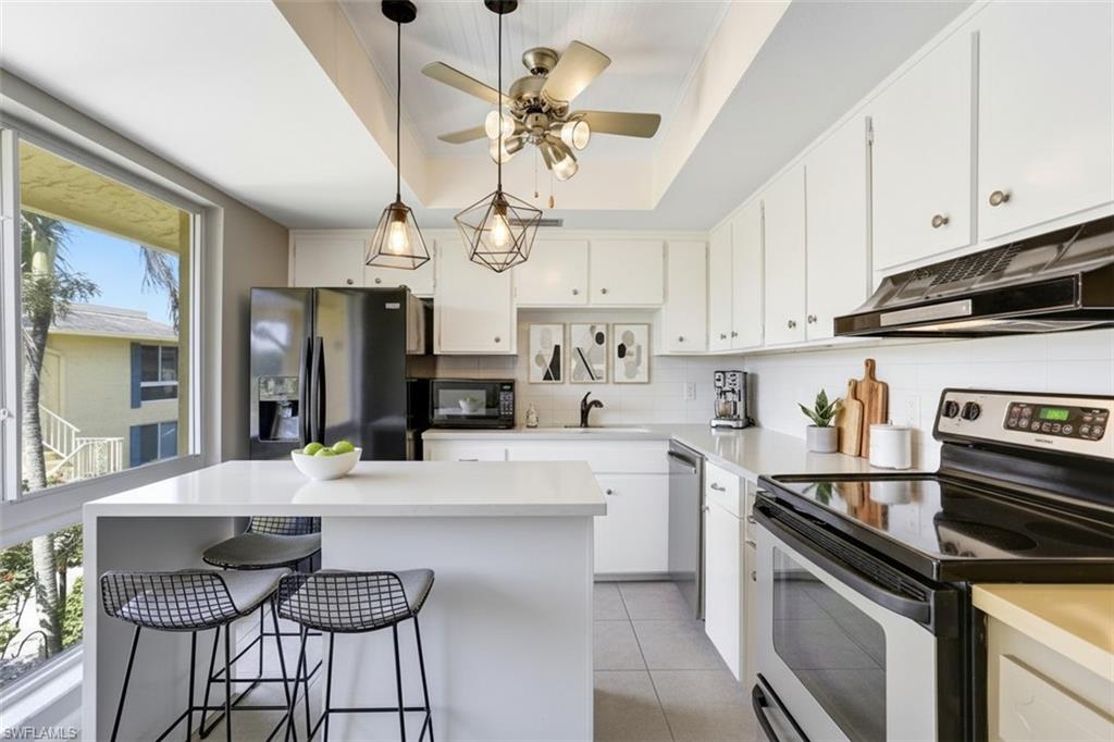 355 Palm Drive, Unit 732 Naples, FL 34112 - Photo 13 of 50 355-Palm-Dr-732-Naples-FL-Kitchen-virtual staged- featuring black appliances, light countertops, white cabinetry, a kitchen island, and hanging light fixtures