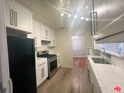 a kitchen with granite countertop a refrigerator a stove and white cabinets with wooden floor
