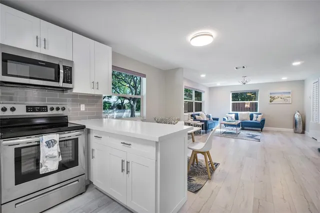 a kitchen with stainless steel appliances granite countertop a stove top oven a sink dishwasher and white cabinets with wooden floor