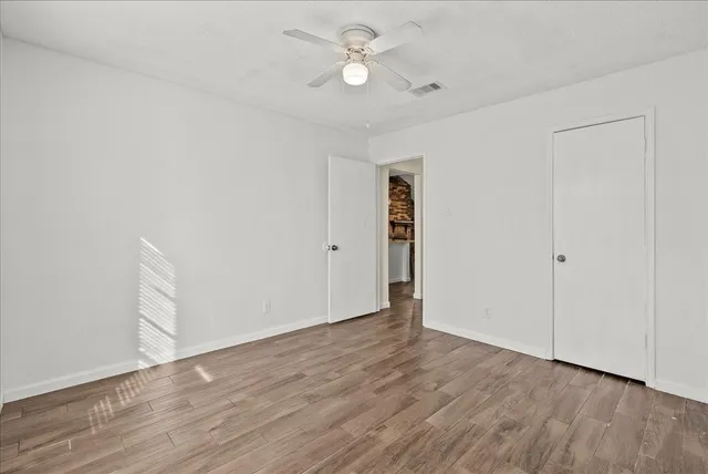 an empty room with wooden floor ceiling fan and refrigerator