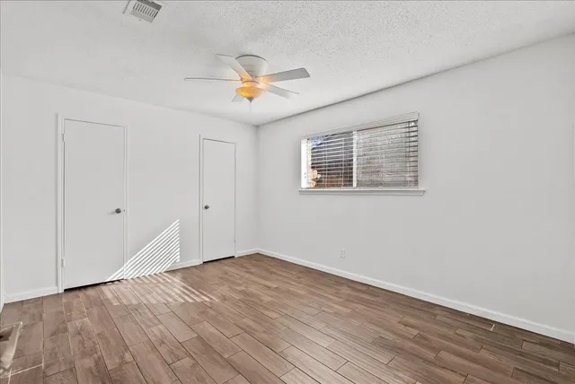an empty room with wooden floor fan and windows