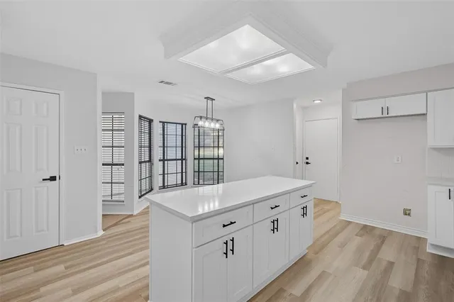 a hall with kitchen island white cabinets and wooden floor