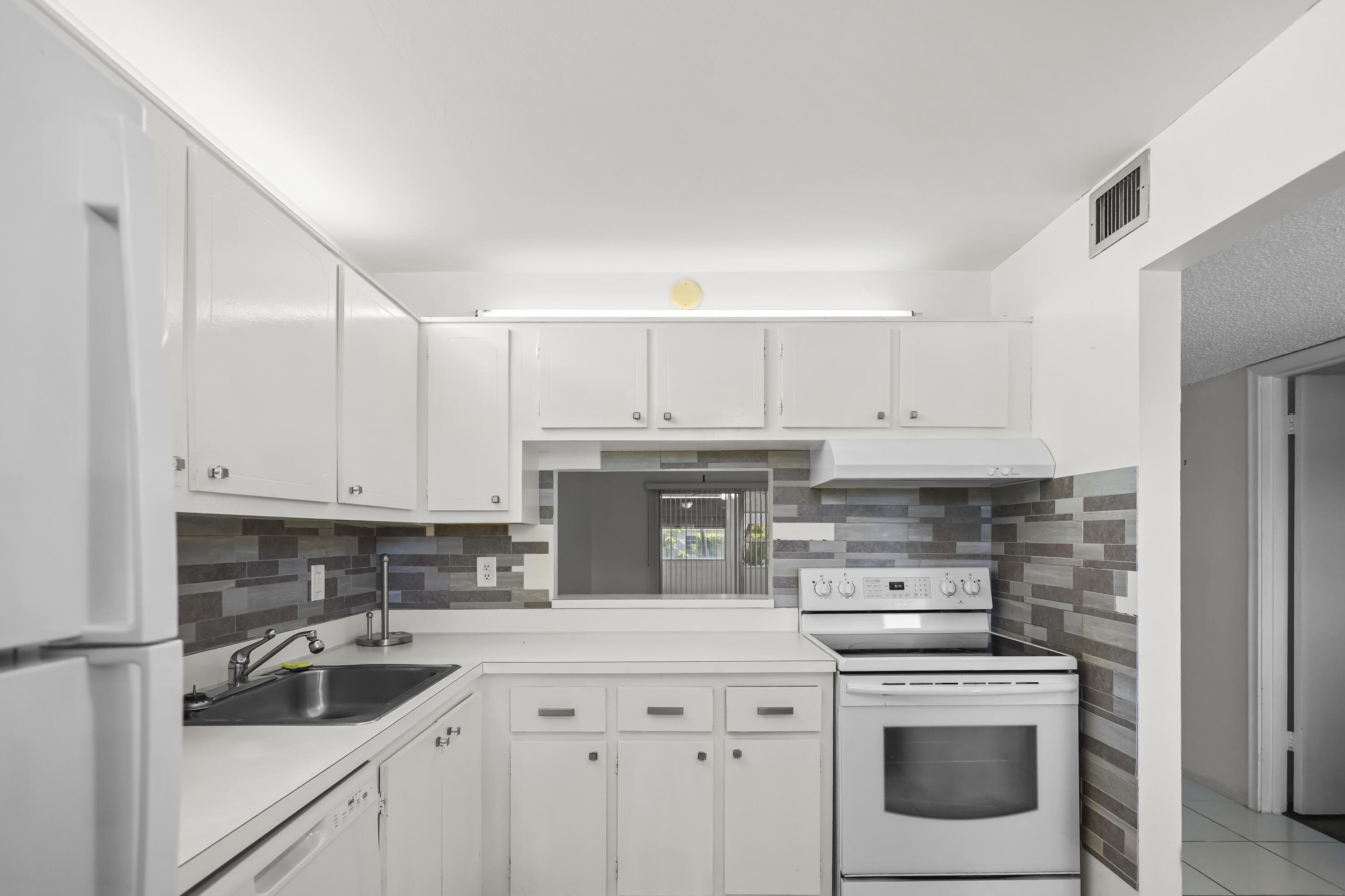 2500 Fiore Way, Unit 103 Delray Beach, FL 33445 - Photo 6 of 19 a kitchen with white cabinets sink and stainless steel appliances