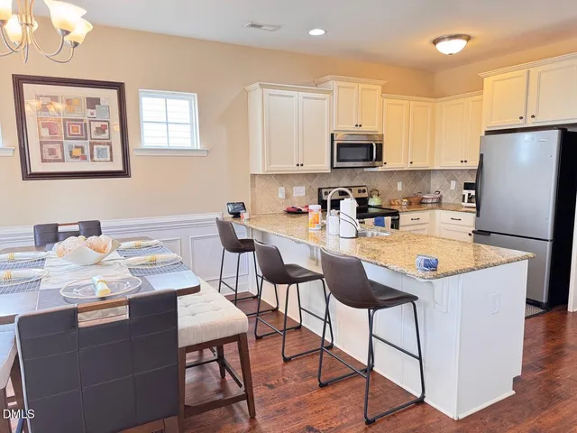 a kitchen with stainless steel appliances granite countertop a stove a refrigerator a sink a stove a dining table and chairs with wooden floor